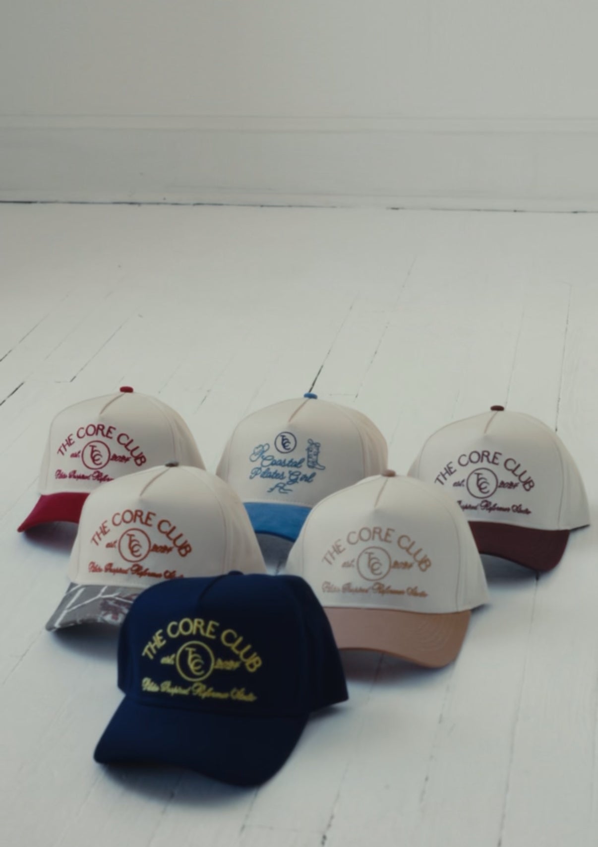 Collection of TCC core club pilates baseball caps with 'The Core Club' logo on a white surface, accessory for lounging, running errands, or working out doing pilates 