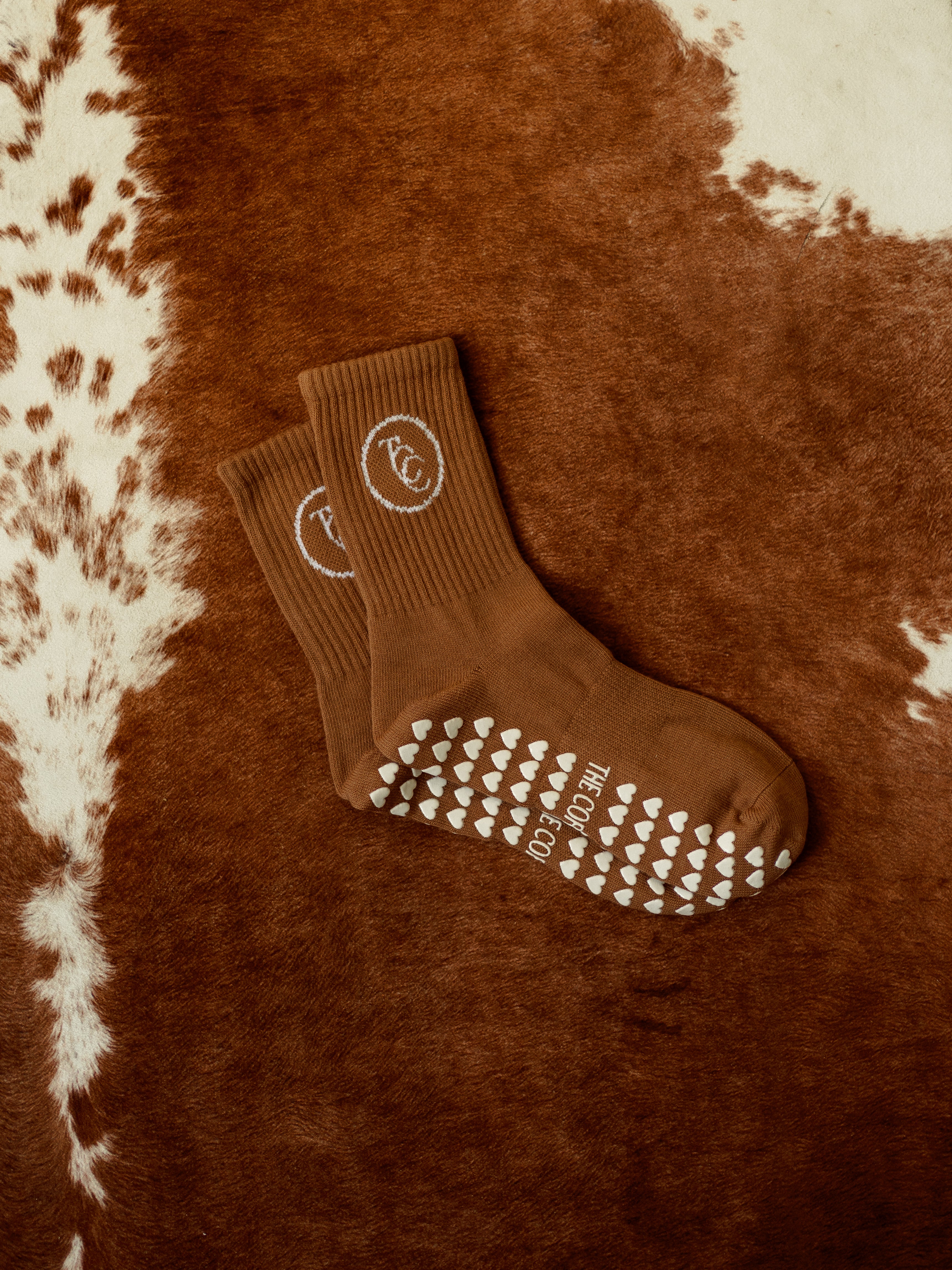 TCC Original Round Logo Grip Socks – jacquard logo Pilates socks in tan, black & white. Dot or heart grippies, one-size-fits-all, studio-ready style.